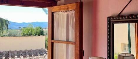 A room with a wooden-framed window, a table with a lamp, and a mirror on the wall.