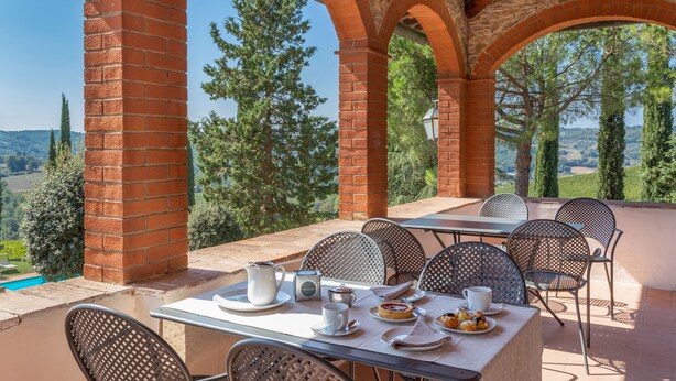 An outdoor patio with a table set for dining, surrounded by brick arches and metal chairs, overlooking a scenic landscape. - Fattoria Pratale (Barberino Tavarnelle)