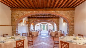 A dining area with multiple tables set for a meal, stone arches, and a view of the outside. - Fattoria Pratale (Barberino Tavarnelle)