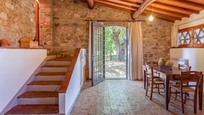 A rustic stone interior with a wooden staircase, a dining area with a table and chairs, and a large open door leading outside. - Fattoria Pratale (Barberino Tavarnelle)