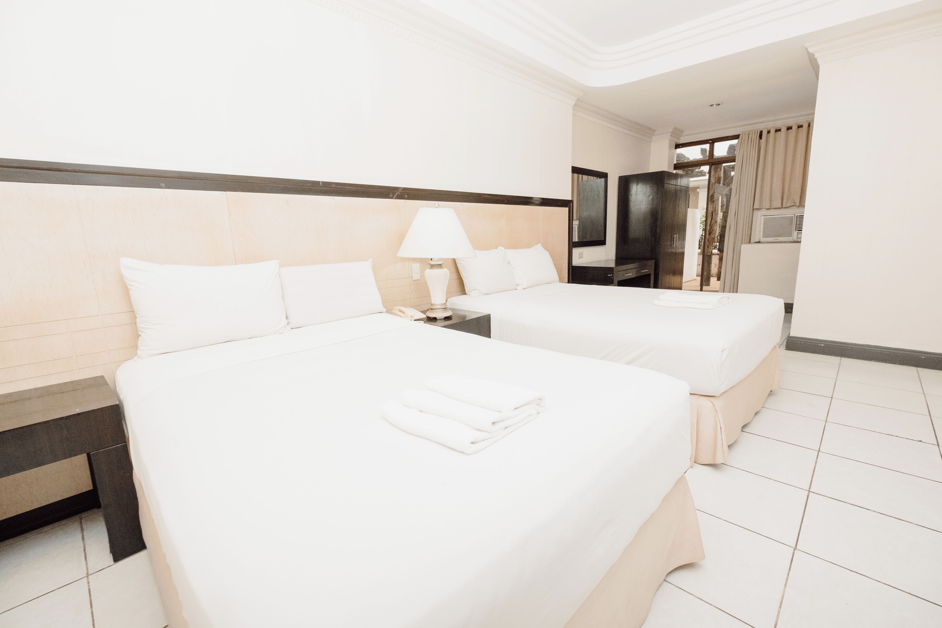 A hotel room with two beds, a TV, and a window with curtains.