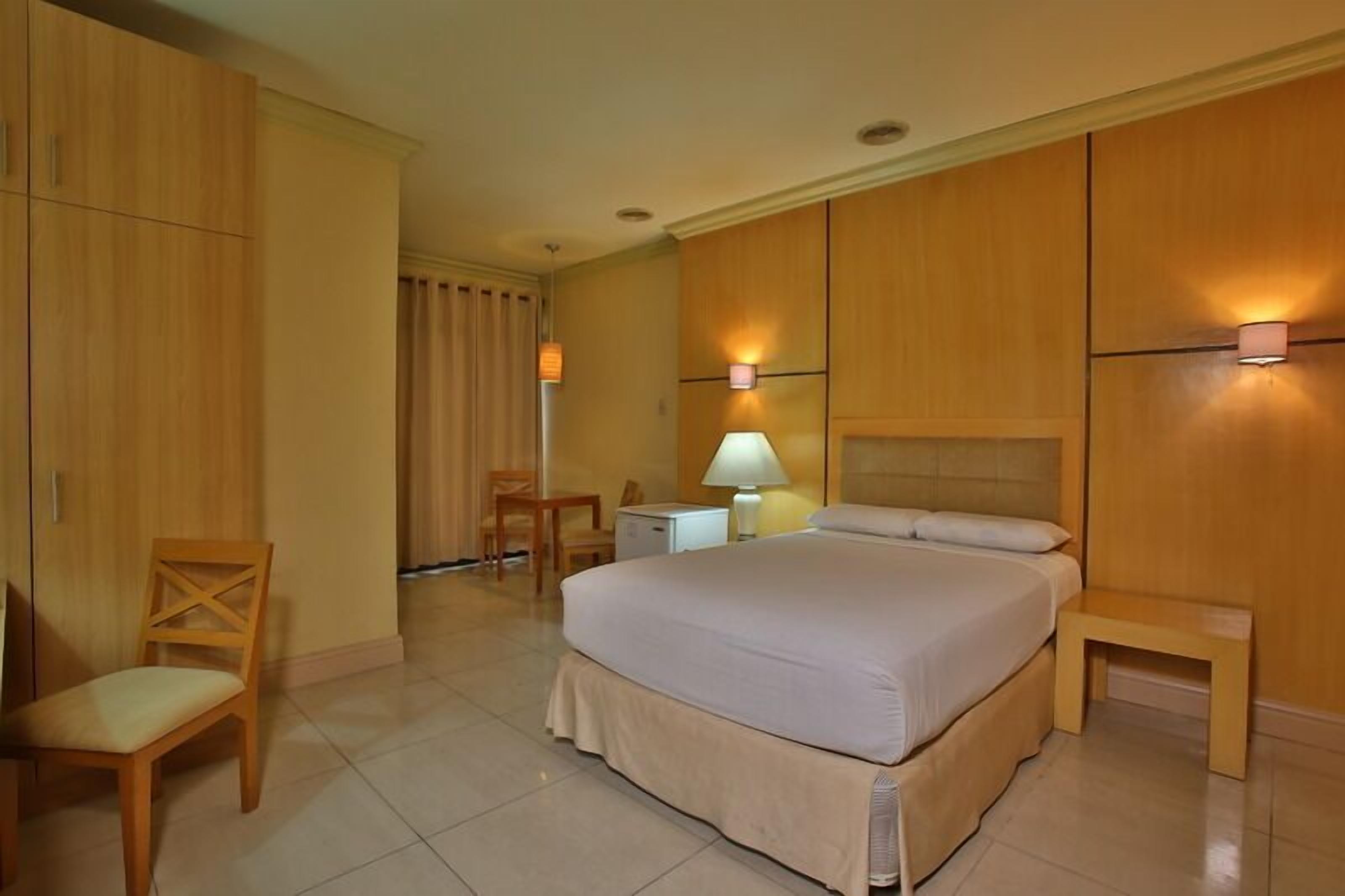 A hotel room with a large bed, a chair, a desk, and a lamp.