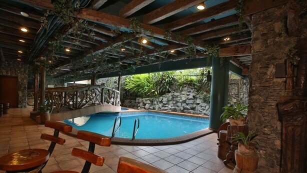 Une piscine intérieure avec des bancs en bois et des murs en pierre.