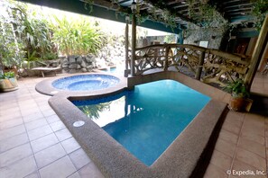 An indoor swimming pool with a stone wall and wooden bridge, surrounded by potted plants and a stone bench. - Crown Regency Residences - Cebu (Cebu City)