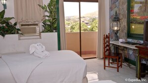 Une chambre d’hôtel avec un lit, un bureau et une chaise, une fenêtre donnant sur un paysage agréable et une plante en pot.
