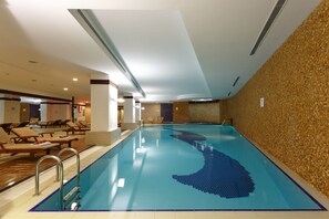 An indoor swimming pool with a blue wave design, lounge chairs, and a tiled wall. - Byotell Istanbul (Istanbul)