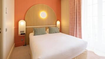 Habitación de hotel con una cama grande, dos lámparas de noche, un espejo redondo sobre la cama y una ventana con cortinas.