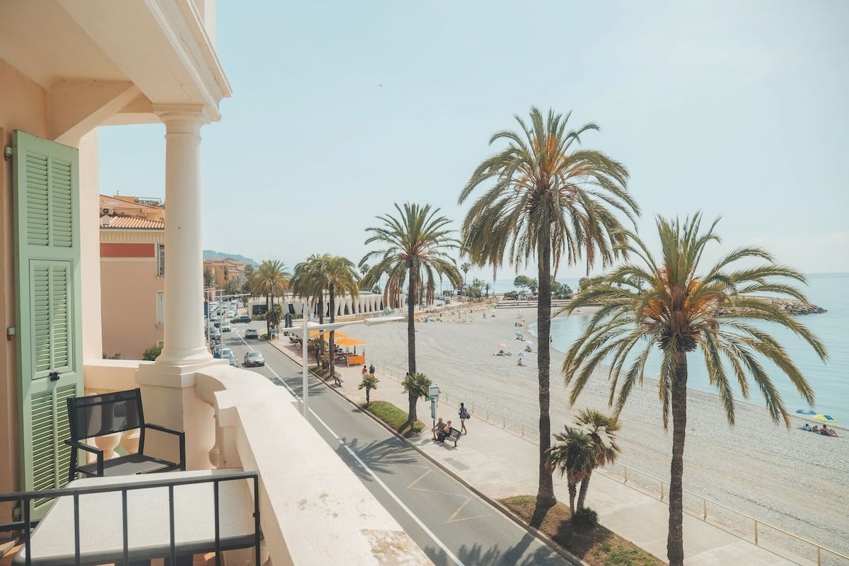 Un balcone con vista sulla spiaggia, palme e una strada con auto.