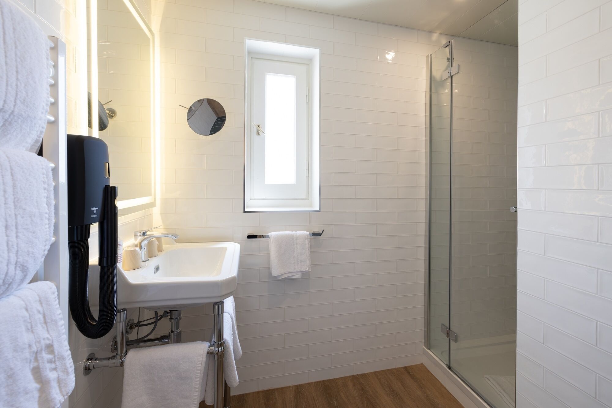 A modern bathroom with a white sink, a handheld showerhead, a glass-enclosed shower, and a towel rack.