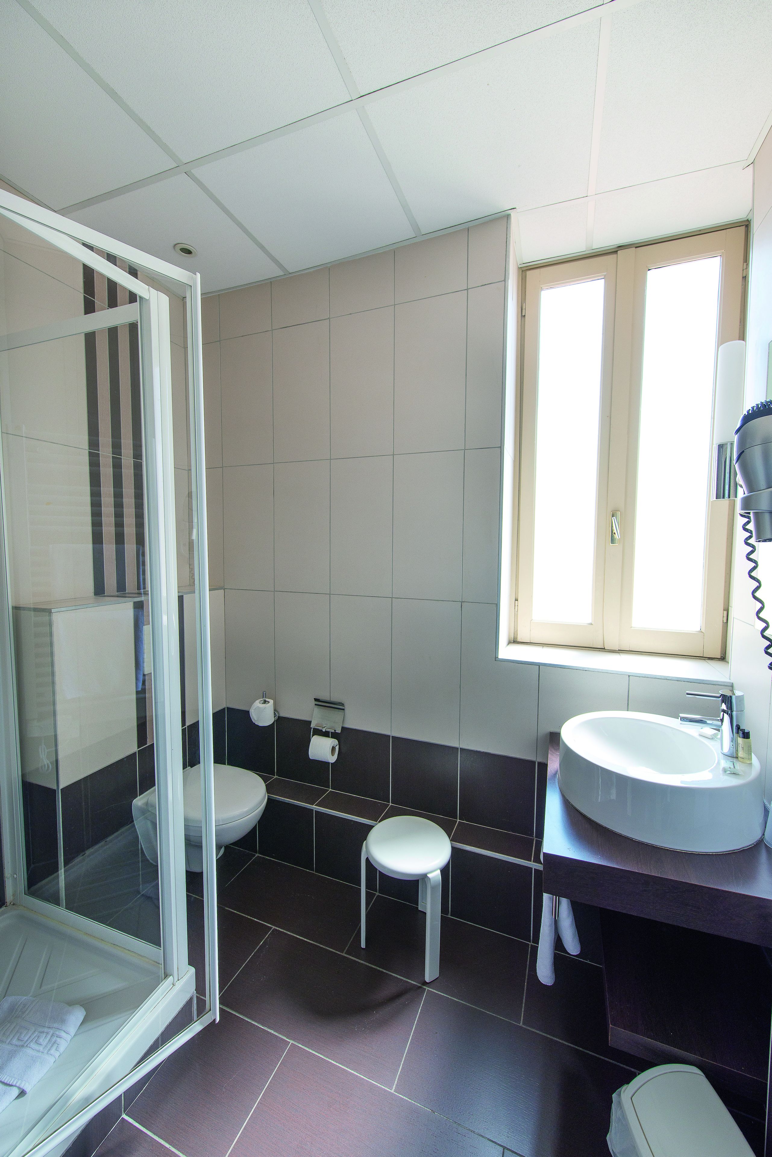 A bathroom with a glass shower enclosure, a toilet, a sink, and a window providing natural light.