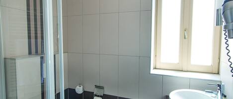 A bathroom with a glass shower enclosure, a toilet, a sink, and a window providing natural light.
