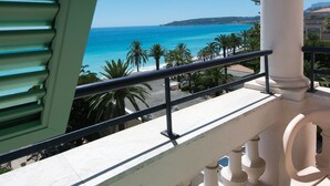 A balcony with a view of the sea, palm trees, and a white column.