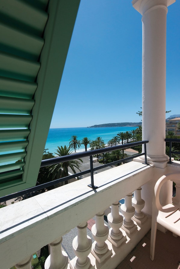 A balcony with a view of the sea, palm trees, and a white column. - Hôtel Vacances Bleues Le Balmoral (Menton)
