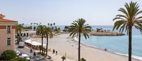 A beach with palm trees, a promenade, and a view of the sea.