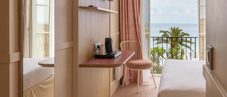 Habitación de hotel con cama, escritorio con silla, televisor y un amplio ventanal con vista al mar.
