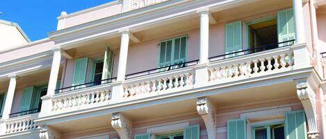 A pink building with balconies and green shutters.