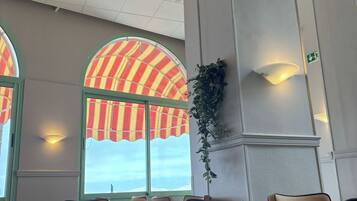 A conference room with a large table, chairs, and a view through a window with striped curtains.
