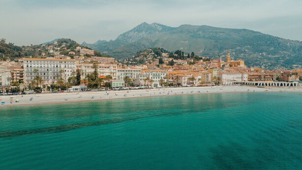 A coastal town with a beach, buildings, and mountains in the background.