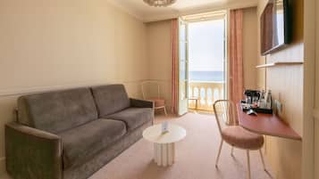 Une chambre d’hôtel avec un canapé, une petite table ronde, une chaise, une télévision et un balcon avec des rideaux.