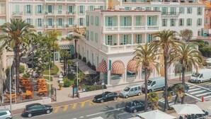 A multi-story hotel with balconies, palm trees, and a view of the surrounding town and mountains.