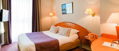 A hotel room with a bed, a desk, a chair, a television, and two wall-mounted lamps.