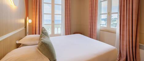 A hotel room with a large bed, two pillows, a bedside table, and a window with curtains.