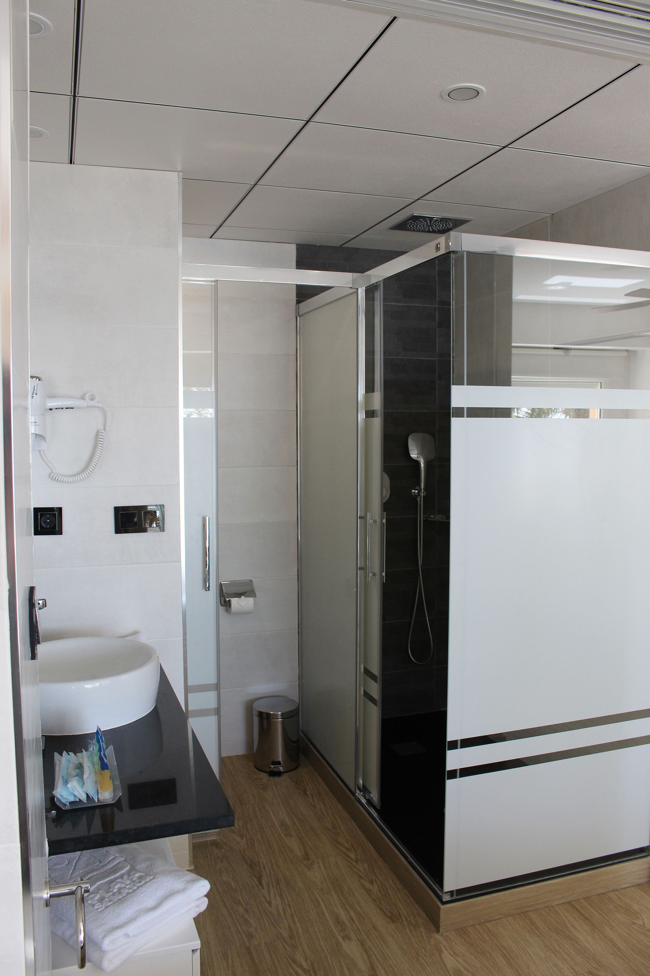 Un baño moderno con lavamanos, espejo, toallero y cabina de ducha de vidrio.