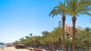 Un hotel frente a la playa, con palmeras, arena y cielos despejados.