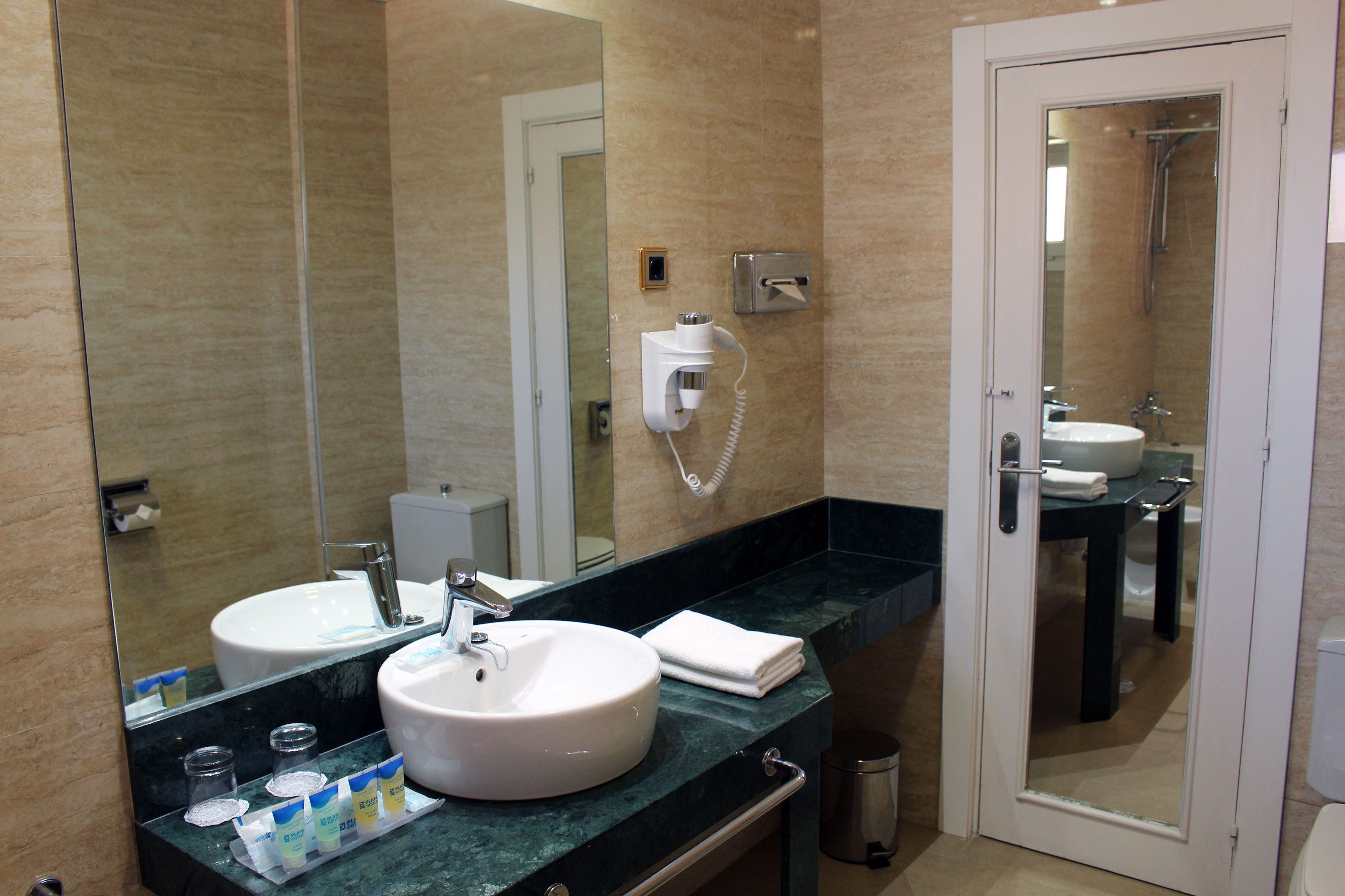 Ein Badezimmer mit großem Spiegel, zwei Waschbecken, einer Handtuchstange und einer Toilette.