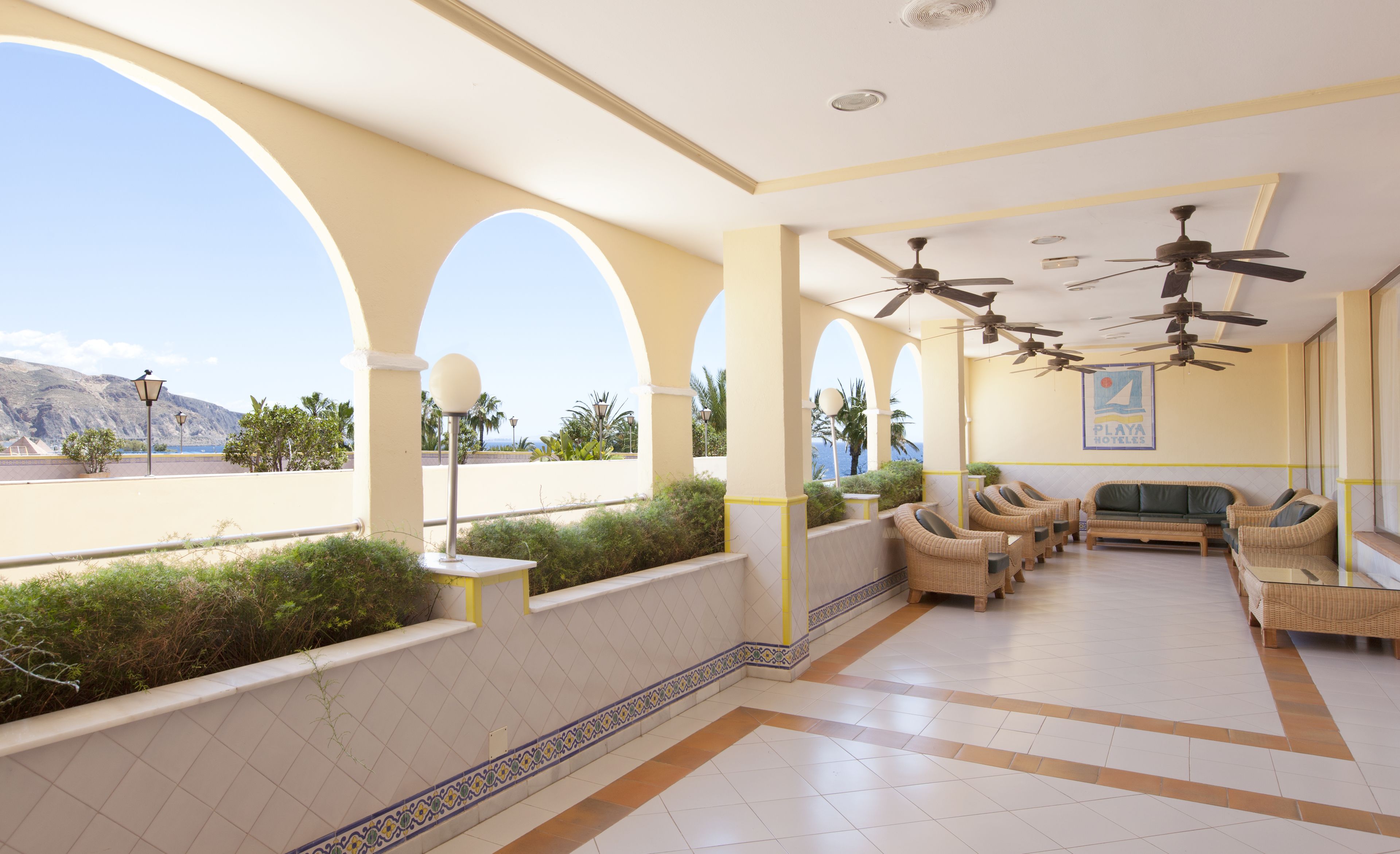 A hotel lobby with a seating area, ceiling fans, and a view of the sea.