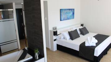 Una habitación de hotel moderna con una cama, una mesita de noche, un ventilador de techo y un baño con bañera y una pequeña planta.