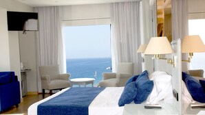 Habitación de hotel con una cama grande, dos sillones, una mesita y vistas al mar.
