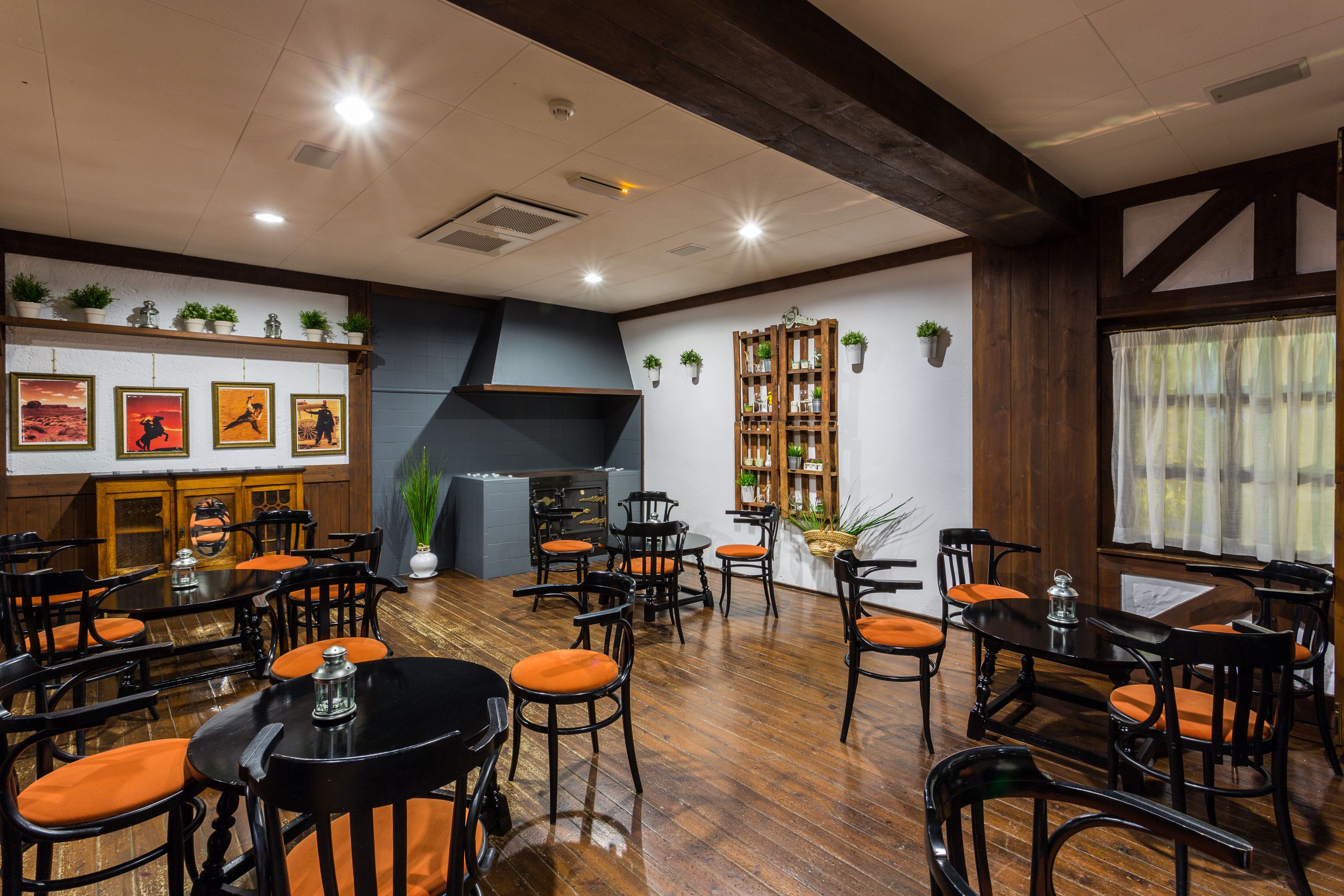 A restaurant with wooden floors, black and orange chairs, and a large wooden bookshelf.