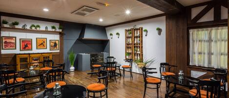 A restaurant with wooden floors, black and orange chairs, and a large wooden bookshelf.