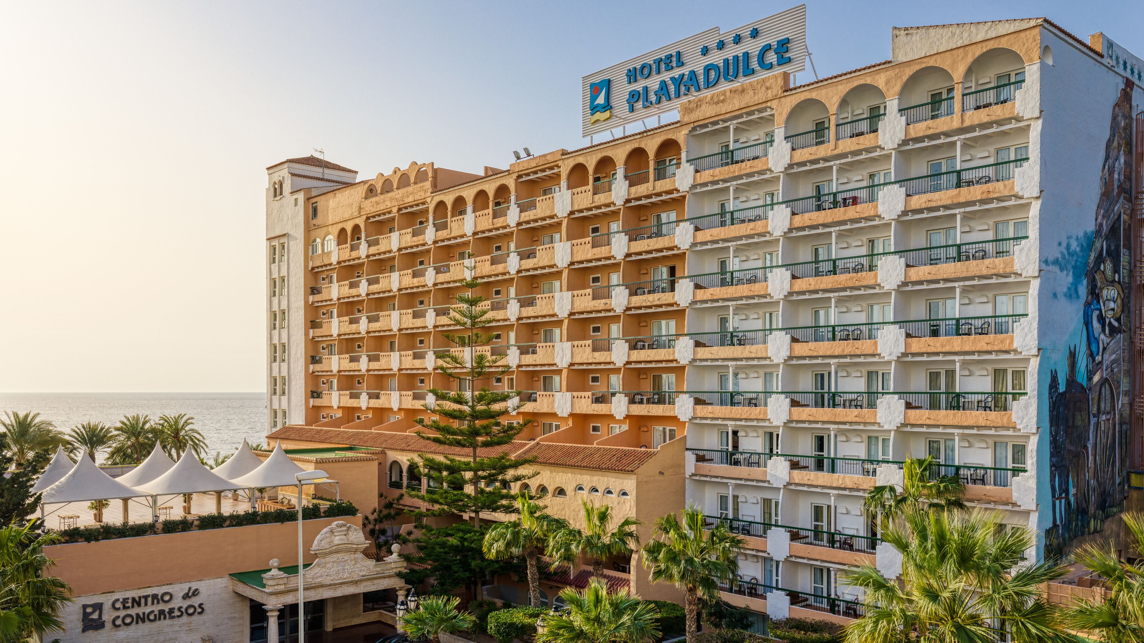 A multi-story hotel with balconies, a beach view, and a mural on the side.