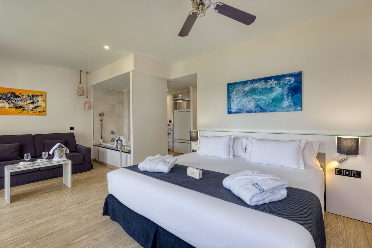 Ein modernes Hotelzimmer mit einem großen Bett, einer Couch, einem Glastisch und einem Deckenventilator.