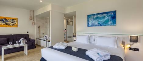 A modern hotel room with a large bed, a sofa, a glass coffee table, and a ceiling fan.