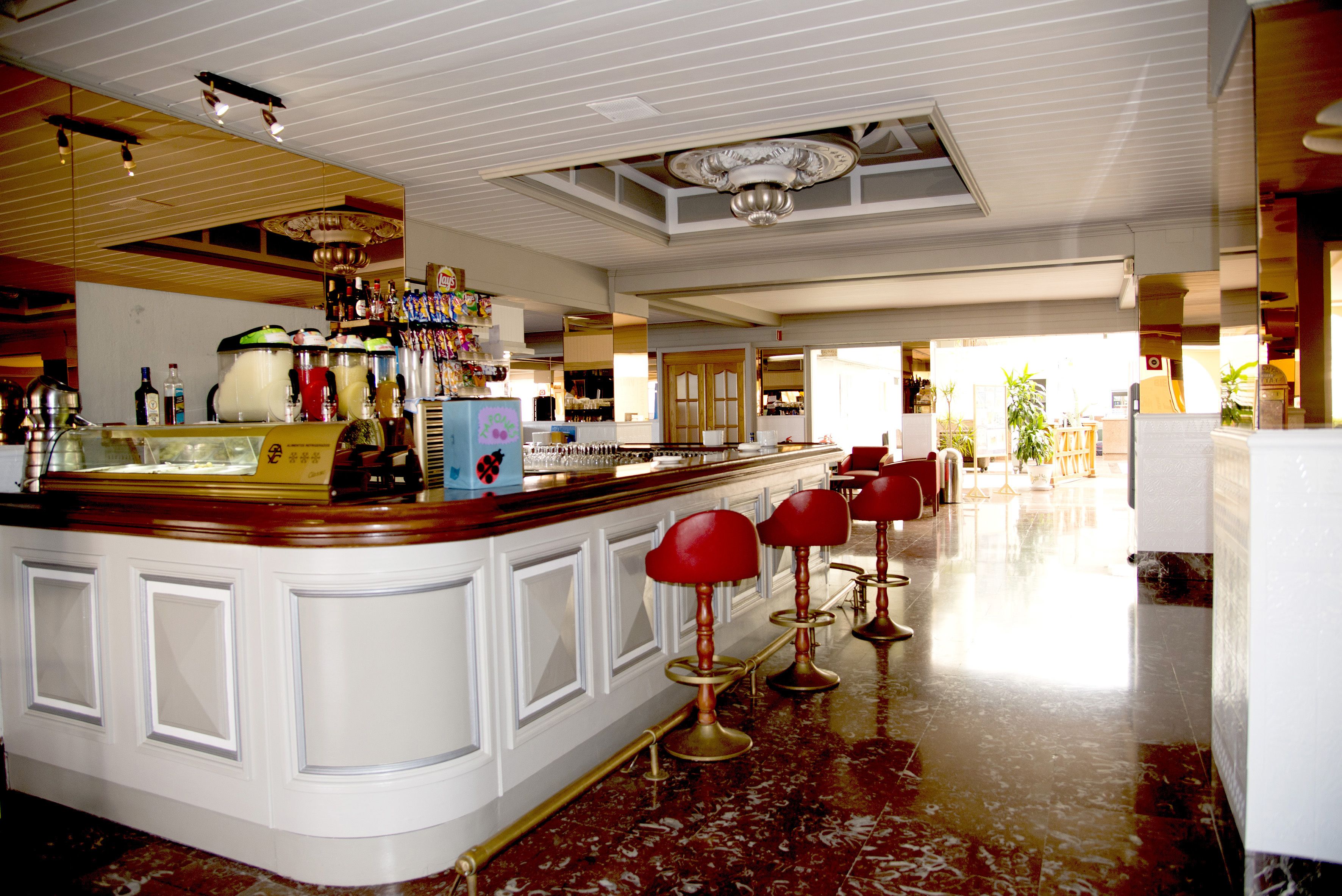 A bar area with a marble floor, white bar counter, and red bar stools.