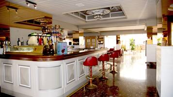 Angolo bar con pavimento in marmo, bancone bianco e sgabelli rossi.