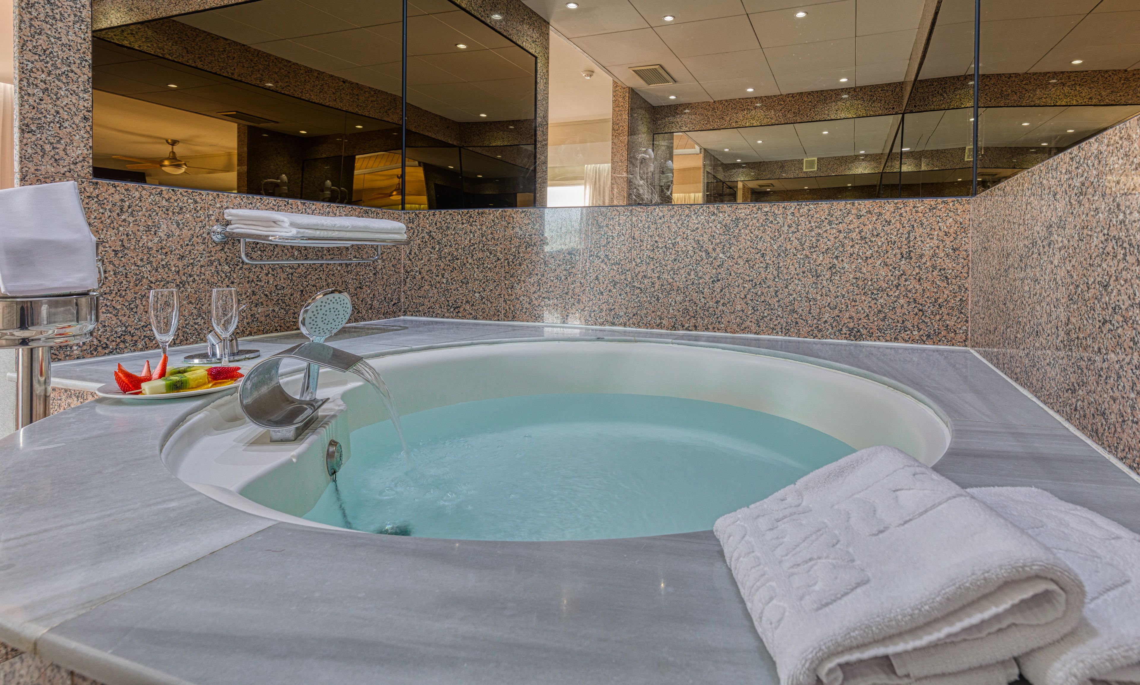A modern bathroom with a large bathtub, marble walls, and a glass shower enclosure.