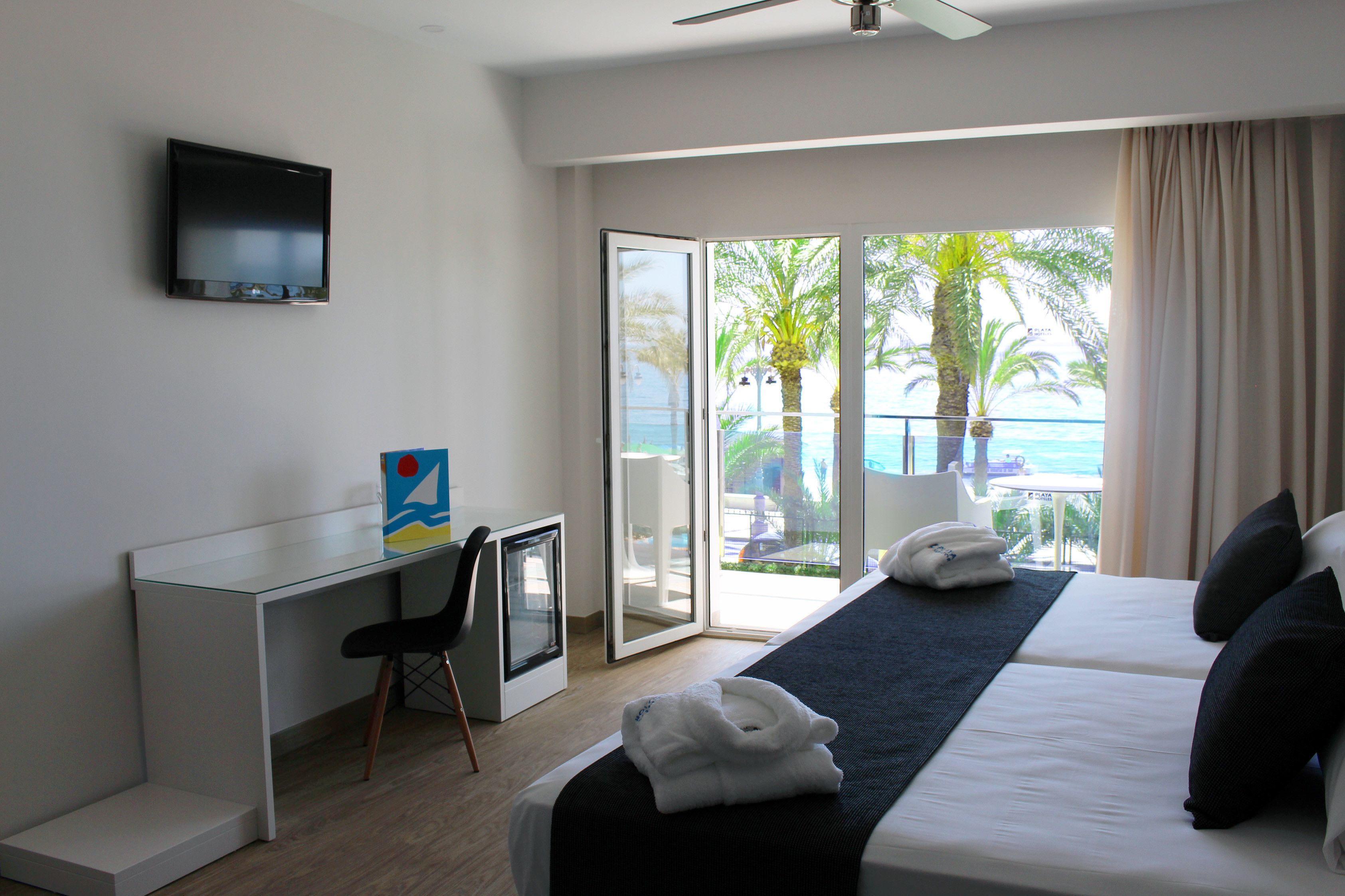 Camera d'albergo con un letto, una scrivania, una sedia, una TV a schermo piatto e una porta scorrevole in vetro che dà su un balcone con vista su palme e sull'oceano.