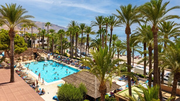 Zona de piscina de un resort con varias piscinas, palmeras y acceso a la playa.
