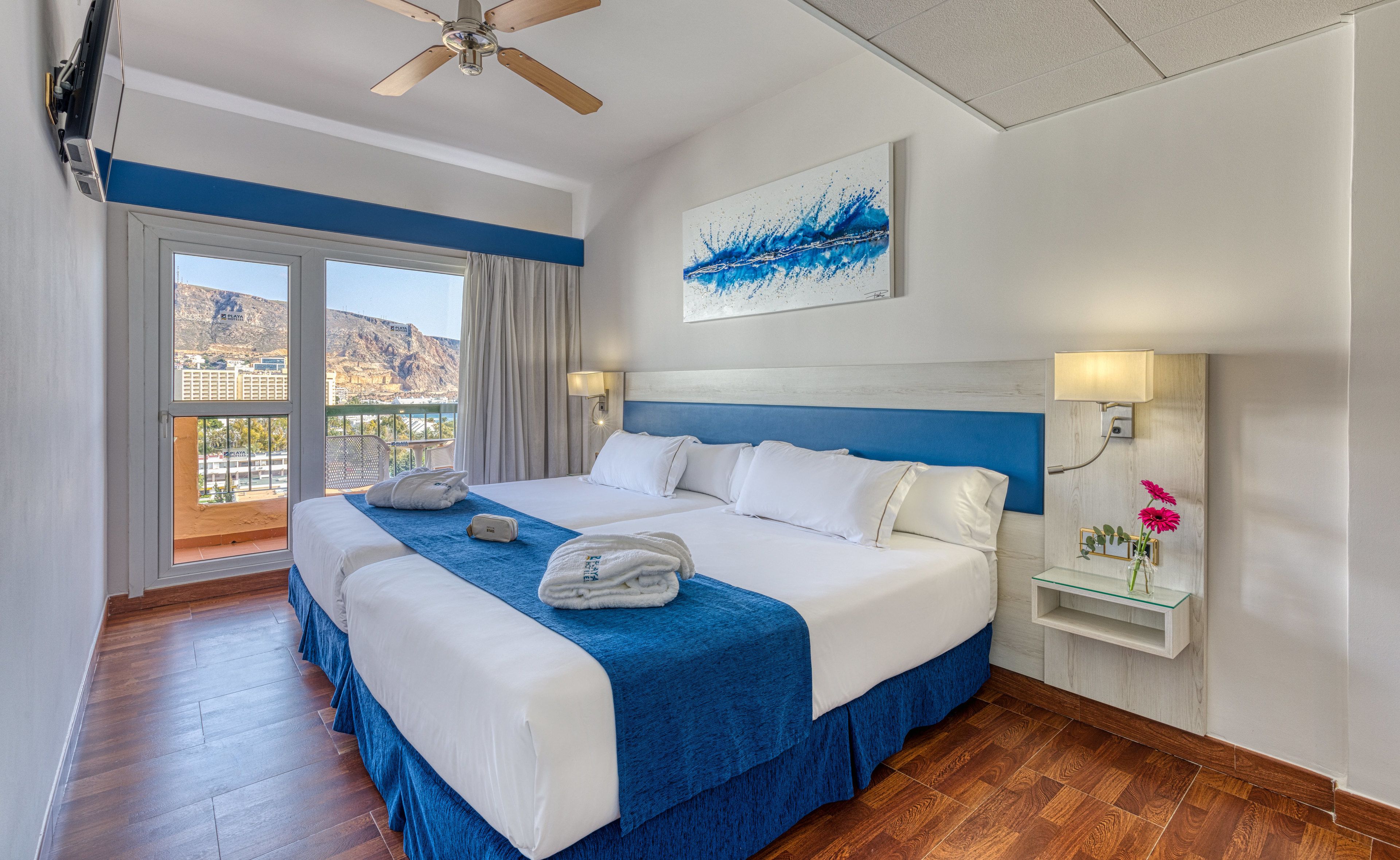 Une chambre d’hôtel avec un grand lit, un ventilateur de plafond, une vue sur les montagnes et un balcon équipé d’une table et de chaises.