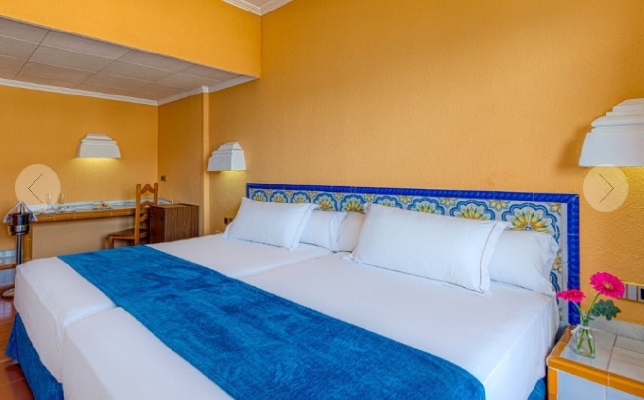 Een hotelkamer met een bed, nachtkastje, spiegel en een wandklok.