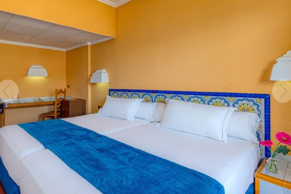 Een hotelkamer met een bed, nachtkastje, spiegel en een wandklok.