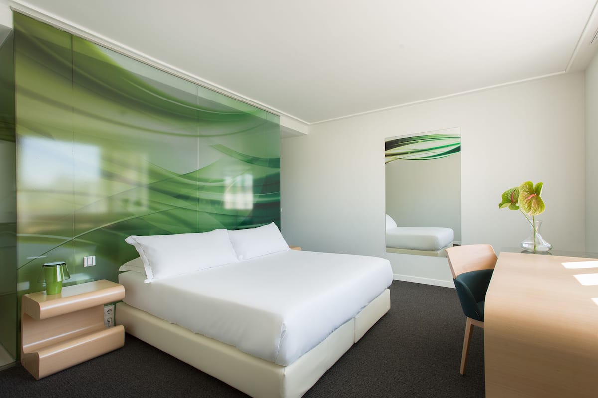 A modern hotel room with a large bed, a desk, and a chair.