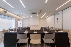 Un salón de conferencias con una larga mesa, sillas, botellas de agua y una pantalla de proyector.