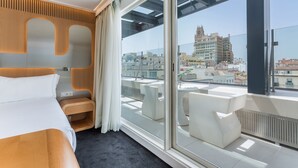 Habitación de hotel moderna con un ventanal grande, una cama, una pequeña zona de estar y vistas a la ciudad.