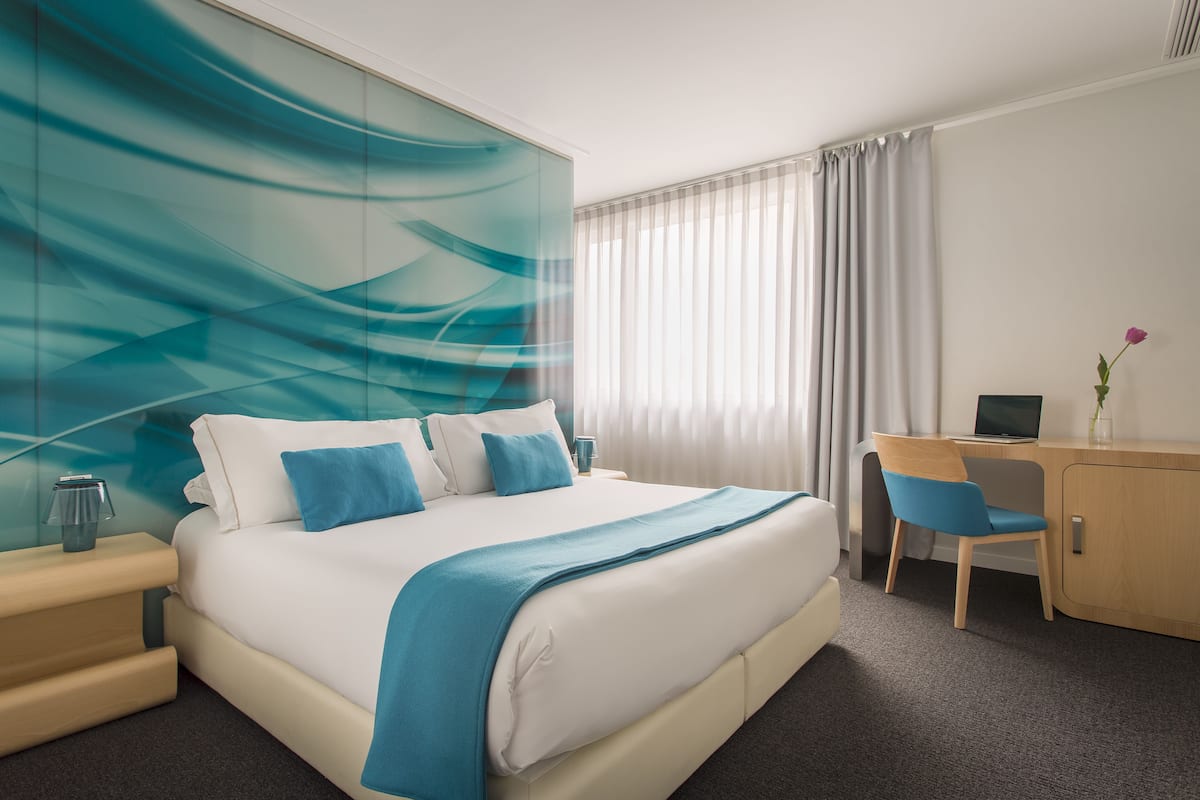 A modern hotel room with a large bed, a desk, and a computer.