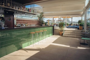 Una zona de bar con pared de azulejos verdes, taburetes y vistas a la ciudad a través de amplias ventanas.